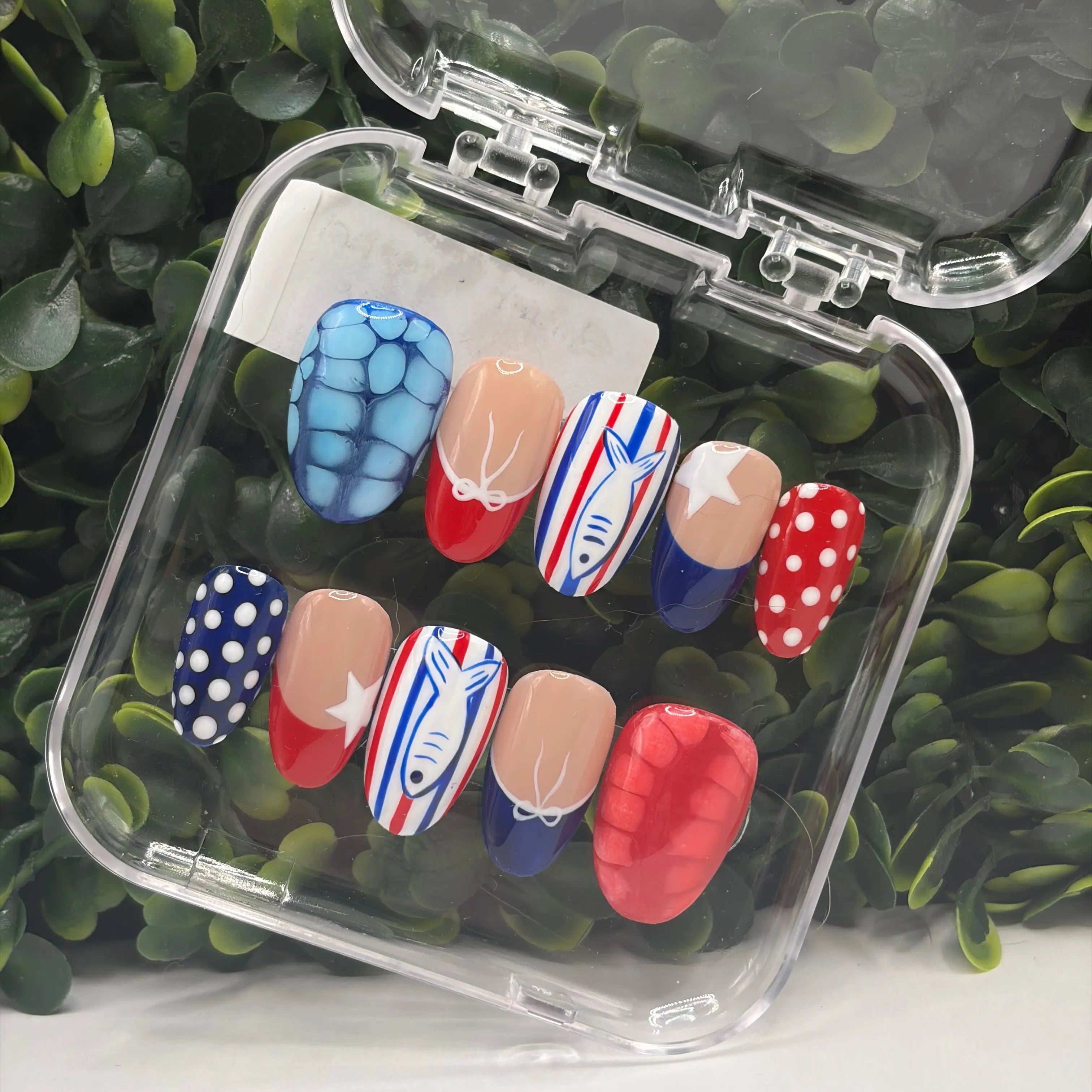 Set of colorful nail art designs in a clear case on a green leafy background